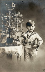 An old, black and white photo of a happy boy with a table top Christmas tree, gifts, and vintage toys, circa 1900.