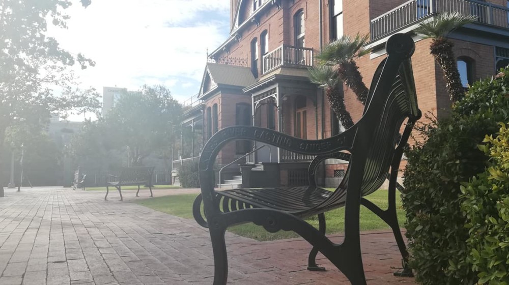 A picture of a park bench at Heritage Square with the south side of Rosson House in the background.