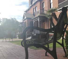 A picture of a park bench at Heritage Square with the south side of Rosson House in the background.