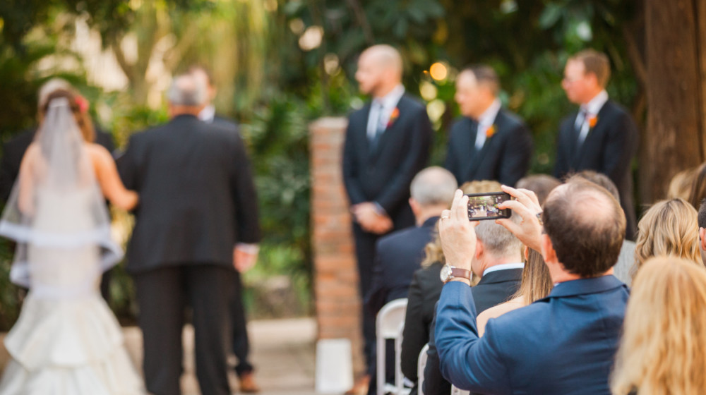 A wedding guest takes a photo of the bride and groom during their wedding at Heritage Square.