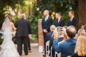 A wedding guest takes a photo of the bride and groom during their wedding at Heritage Square.