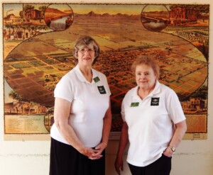 Longtime Heritage Square volunteers Liz and Pat, posing in front of a map of Phoenix from 1895.