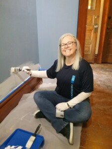 A Heritage Square volunteer smiling as she paints a wall in an exhibit space.