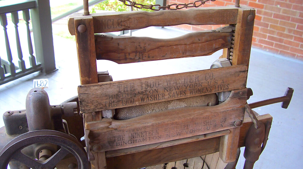 A wood and cast iron 1900 Company Washing Machine, motor operated, with the slogan, “The 1900 Washer Saves Women’s Lives”. It sits on the back porch at Rosson House Museum.