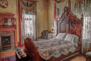 Rosson House's main bedroom, with a fireplace and large, ornate wood bed set.