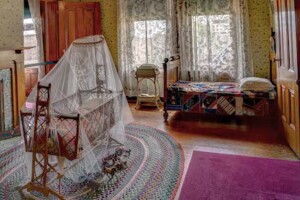 Rosson House Nursery, with an antique toddler-sized bed and wicker cradle with netting over it.