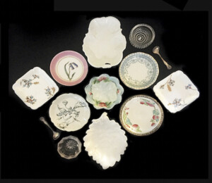 A group of tiny dishes, including, salt cellars (glass) with spoons, bonbon dishes (white, middle top and bottom), a nut dish (center), and butter or condiment dishes.