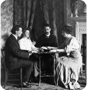 A vintage, black and white photograph of four people sitting around a table, participating in a seance.