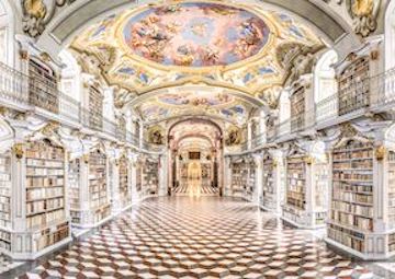 A picture of the Admont Abbey Library, with sun shining in on a checkered tile floor, two stories of rows upon rows of books between columns, and a beautiful painted ceiling.