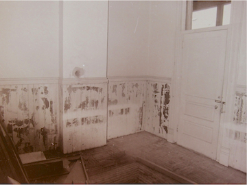 A picture of the Rosson House kitchen during restoration. The walls, door, and wainscotting are painted white, though some of the paint has begun to be removed from the woodwork.