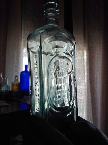 A picture showing the bottle of Dr. Kilmer's Swamp Root on display in the Rosson House Museum doctor's office. It is a large, clear bottle with the name molded directly on the glass with no label. 