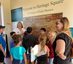 A picture of several students and their chaperone listening to a Heritage Square staff member as they start their field trip at Heritage Square.
