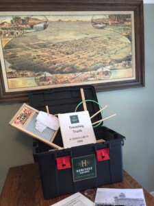 A picture of one of Heritage Square's traveling trunks - the trunk is open and is displaying some of the educational activities, with a wash board, an 19th century game, pictures from the turn of the century, a teachers' binder, and a map of Phoenix in the background circa 1885.