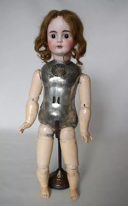 A present day photograph of one of Thomas Edison's talking dolls. Its head, arms, and legs appear to be made of porcelain, but the torso of the doll is made of metal, and there are speaker holes in the chest of the doll.