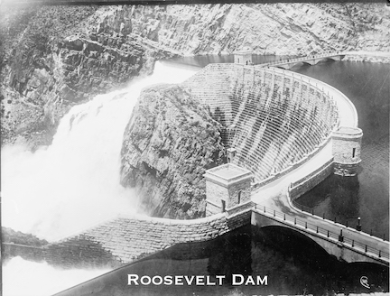 A black and white picture of Roosevelt Dam in Arizona, with water roaring over the spillway to create hydroelectric power.