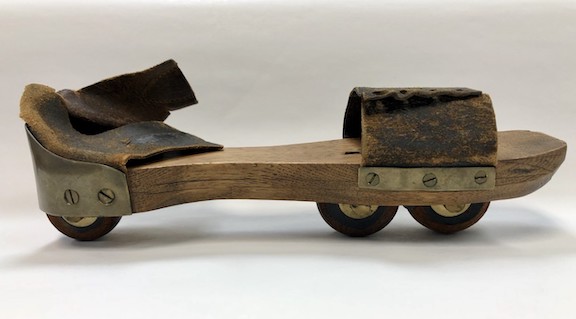 An early roller skate made of wood with three wheels.