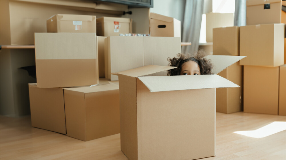 A picture of a child hiding in a large cardboard box, with the top of their head and eyes just peeking up above the edge.