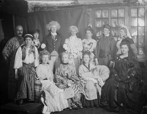 A vintage, black and white photograph of several adults dressed in costume for Halloween, circa 1902.