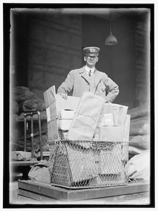 A picture of a postal worker with a stack of boxes in front of him, circa 1913.