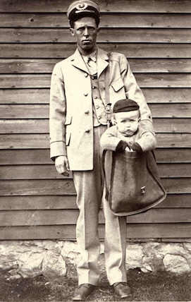 A staged photo of a baby in a letter carrier's mailbag, circa 1913.