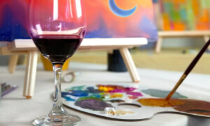 A picture of a glass of wine with a canvas and paints.