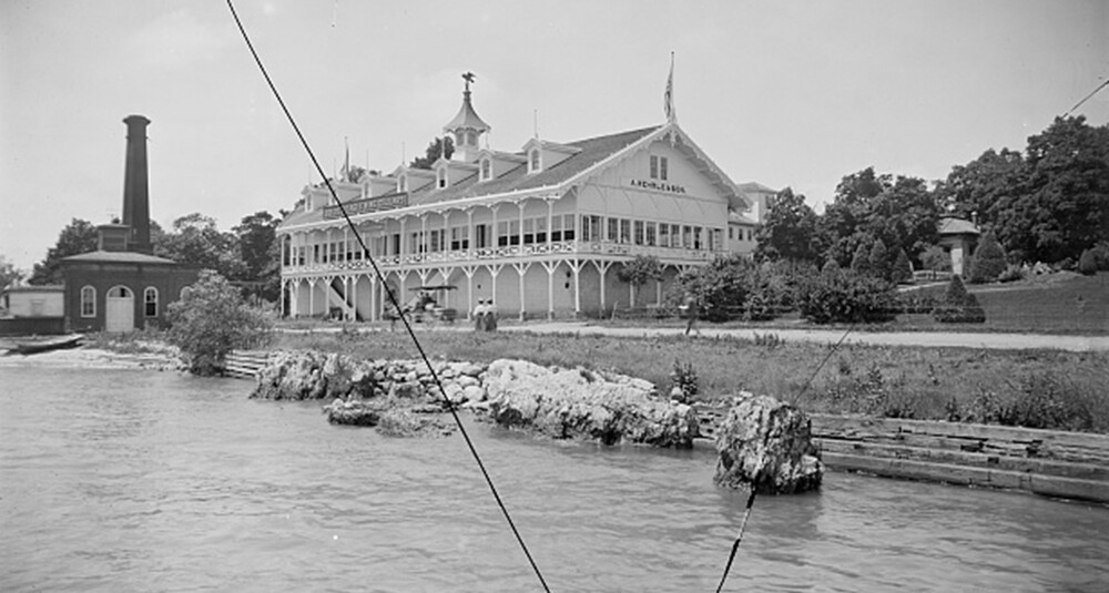 An old, black and white photo with two pictures of a large, two story, white, semi-enclosed dance pavilion on the shore of a lake, circa 1880.